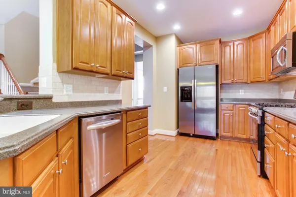 a kitchen with stainless steel appliances granite countertop a refrigerator a sink dishwasher and wooden cabinets with wooden floor
