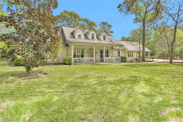 a view of a white house with a big yard and potted plants and large trees