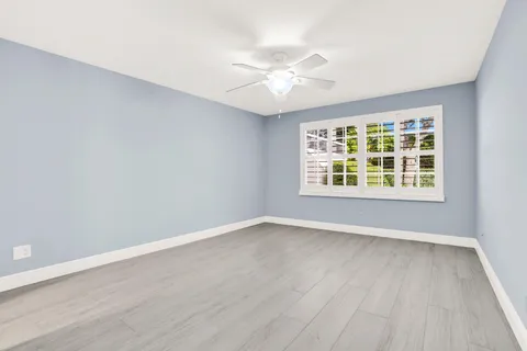 an empty room with wooden floor chandelier fan and windows