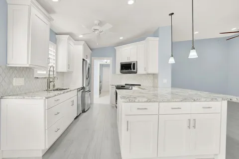 a large white kitchen with kitchen island granite countertop lots of white stainless steel appliances