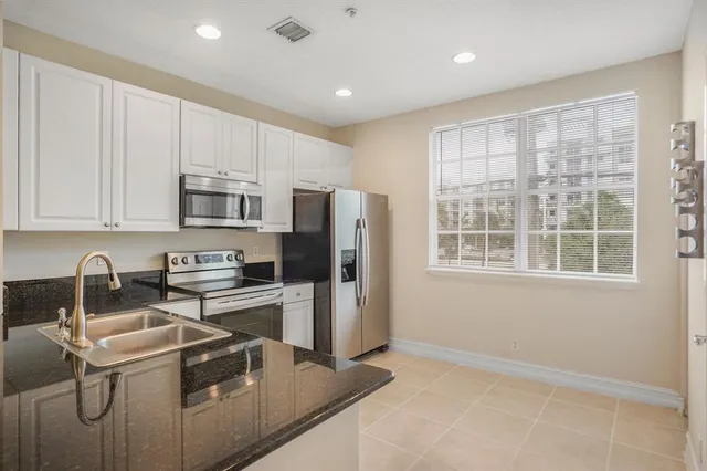 a kitchen with stainless steel appliances granite countertop a stove a sink a refrigerator white cabinets and a refrigerator with wooden floor