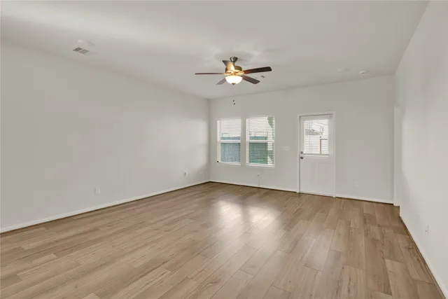 an empty room with wooden floor ceiling fan and windows