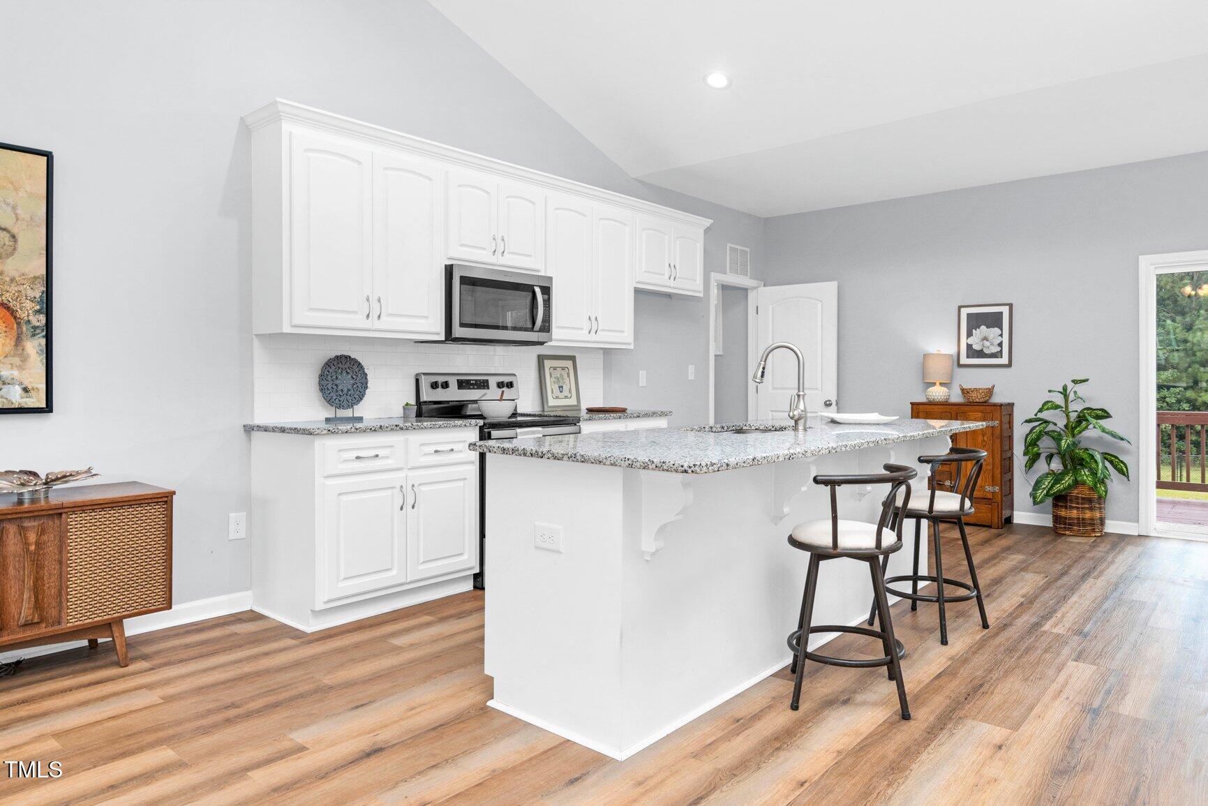 9506 South Beaver Crk Way Middlesex, NC 27557 - Photo 8 of 28 a kitchen with stainless steel appliances granite countertop a stove top oven a sink a dining table and chairs with wooden floor