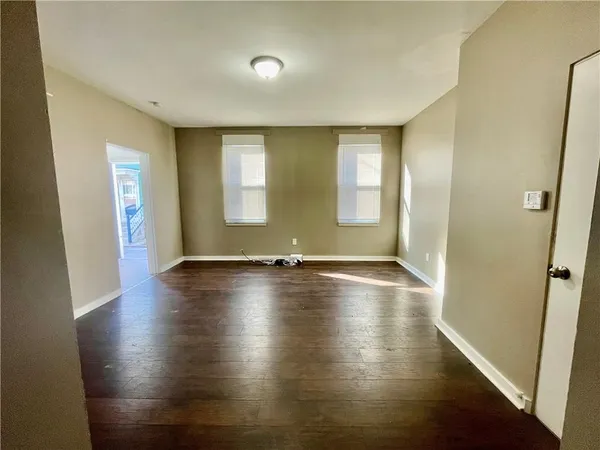 an empty room with wooden floor and windows with curtains