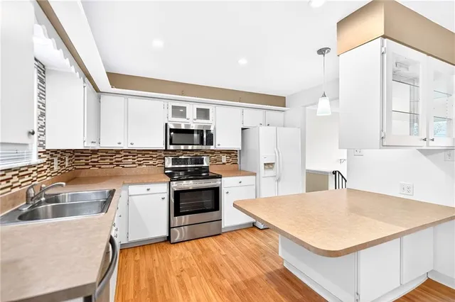 a kitchen with stainless steel appliances a stove a sink dishwasher a refrigerator with white cabinets and wooden floor