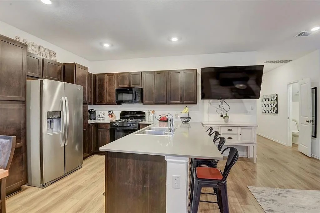 171 Santa Julia Kyle, TX 78640 - Photo 5 of 18 Kitchen featuring dark wood finish cabinetry, black appliances, a breakfast bar area, light wood finished floors, and a peninsula