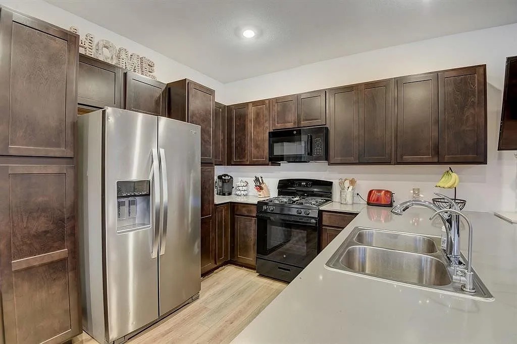 171 Santa Julia Kyle, TX 78640 - Photo 10 of 18 Kitchen featuring black appliances, dark wood finish cabinetry, and light wood-type flooring