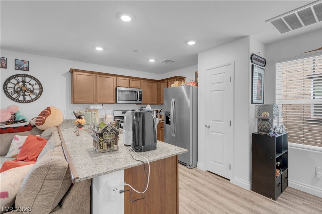 4536 Woolcomber Street Las Vegas, NV 89115 - Photo 19 of 34 Kitchen with a breakfast bar, a peninsula, wood finish cabinetry, stainless steel appliances, and light stone counters