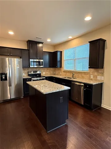 a kitchen with stainless steel appliances granite countertop a stove a refrigerator and a sink with wooden floor