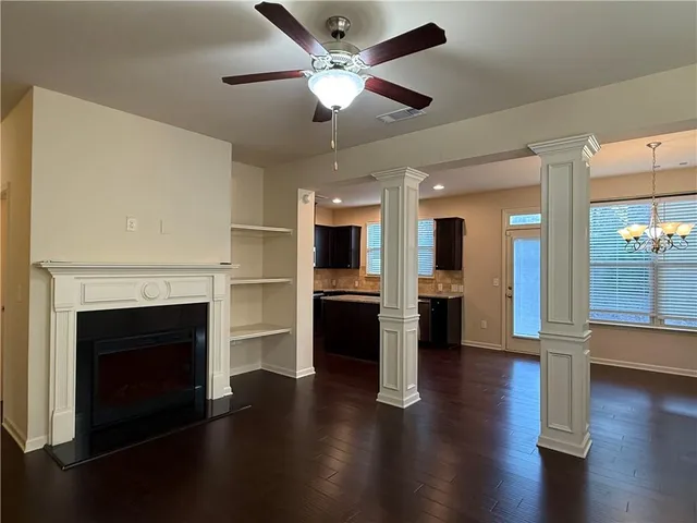 an empty room with wooden floor a fireplace a ceiling fan and a kitchen view