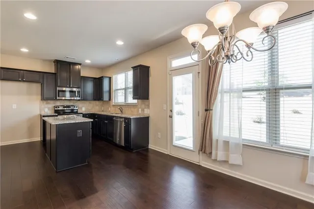 a kitchen with stainless steel appliances granite countertop a refrigerator a sink dishwasher a stove and a dining table with wooden floor