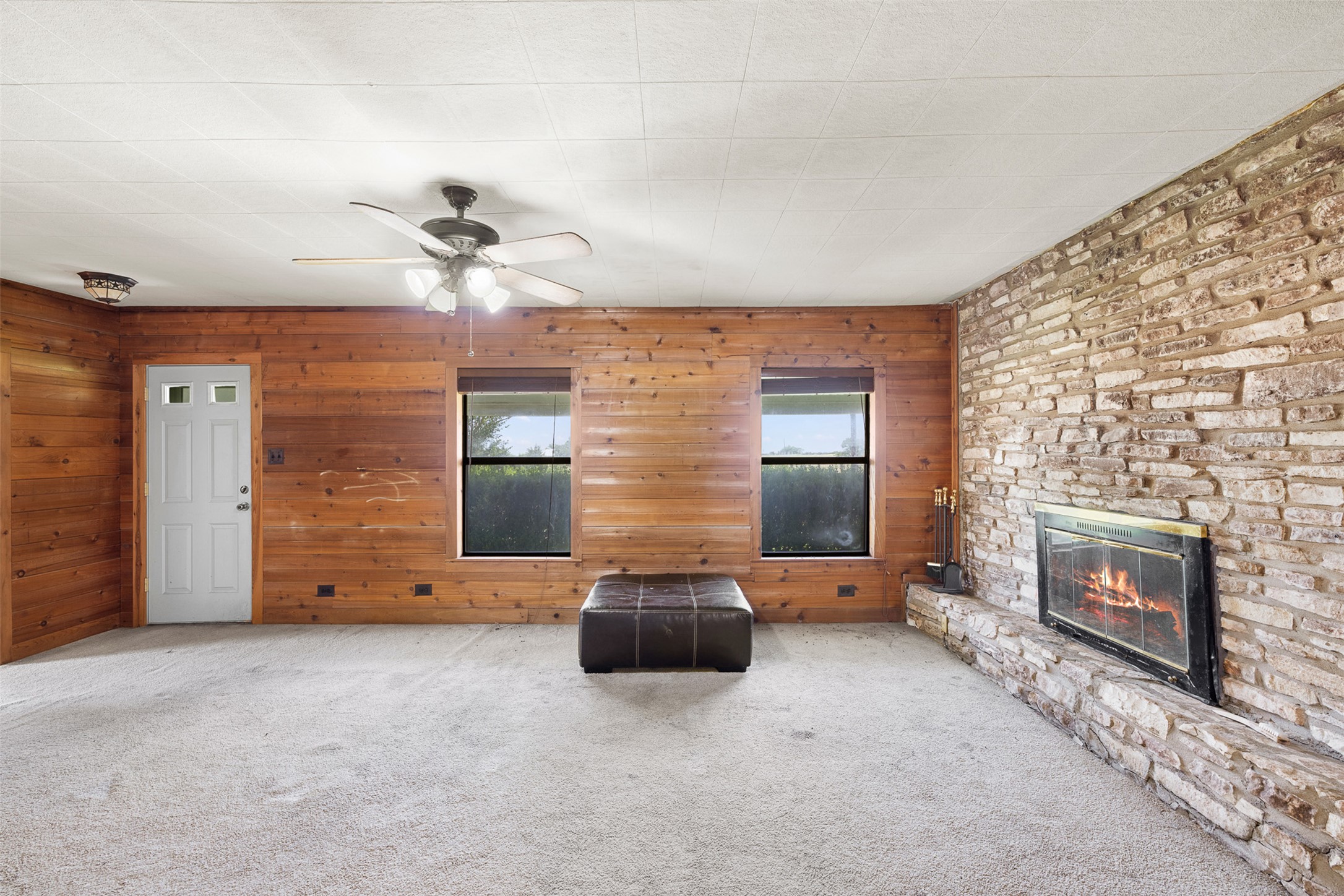 763 Upper Elgin River Road Elgin, TX 78621 - Photo 3 of 40 A cozy living space features wood paneling and a stone fireplace, perfect for relaxation.