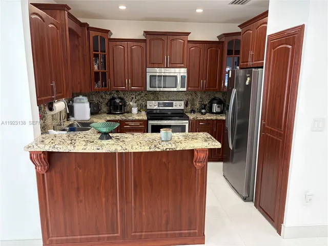 a kitchen with stainless steel appliances granite countertop wooden cabinets a refrigerator and a sink