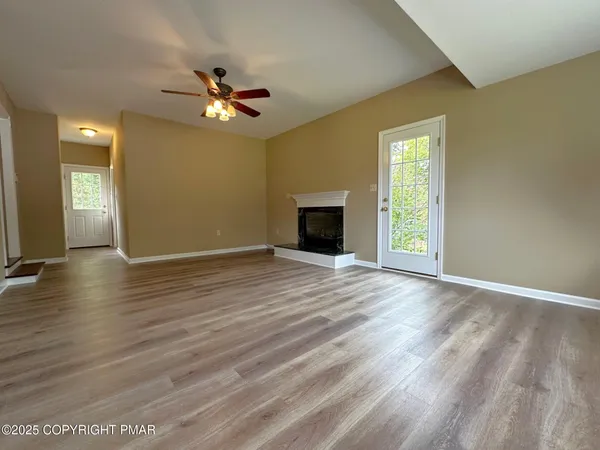 an empty room with wooden floor a ceiling fan and windows