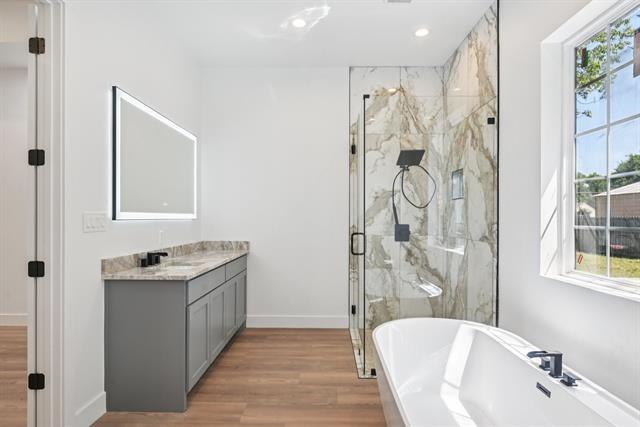 2936 Henry Road Lancaster, TX 75134 - Photo 19 of 28 Freestanding soaking tub, walk-in shower with glass enclosure, single vanity with stone countertop, wood-finish flooring, and a large window