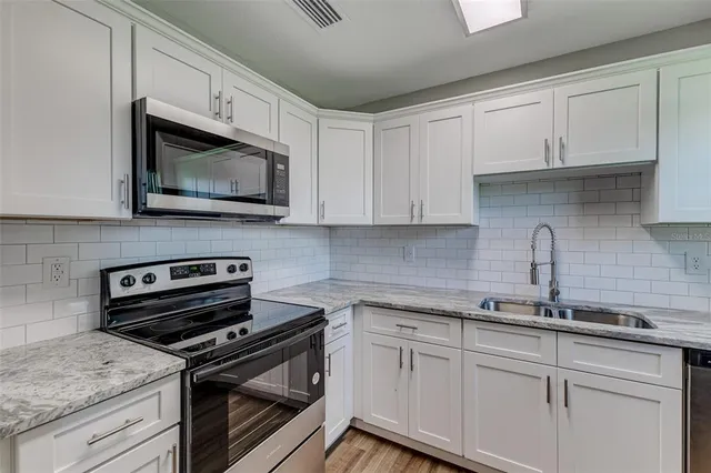 a kitchen with granite countertop white cabinets white stainless steel appliances and a sink