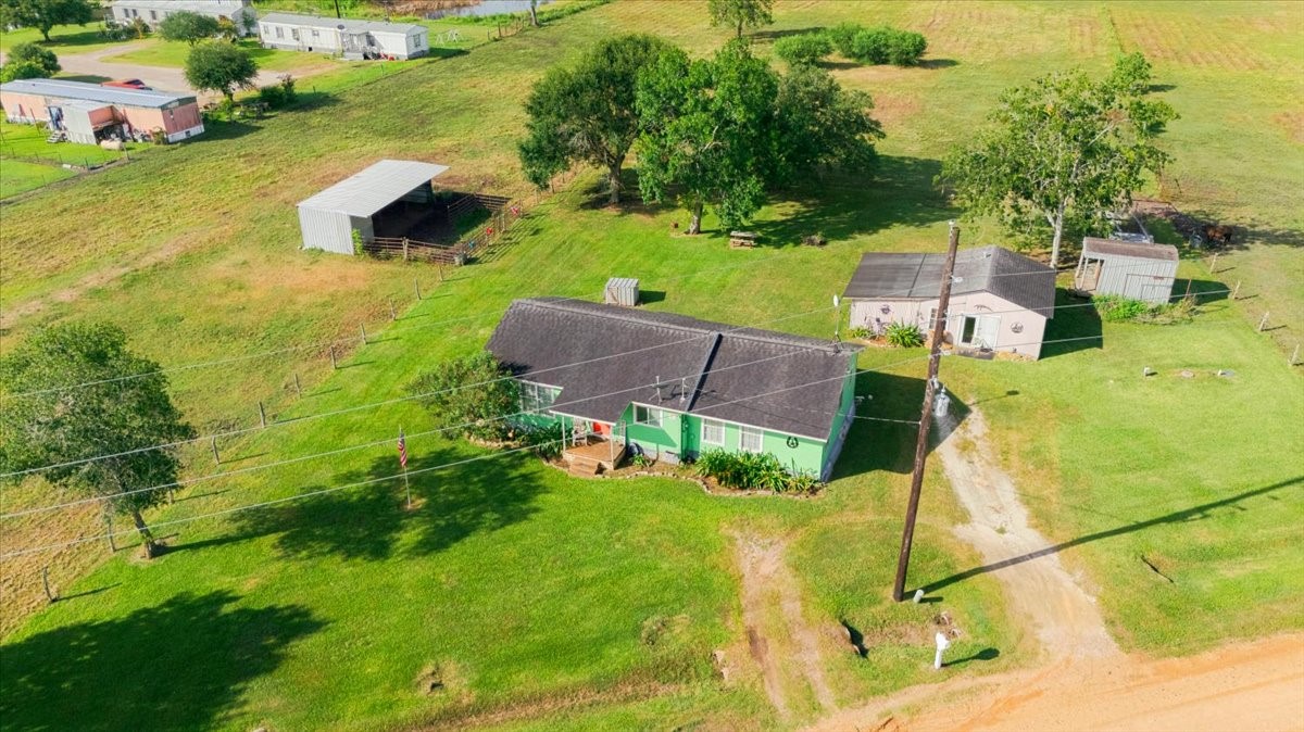 765 Norcross Road Wallis, TX 77485 - Photo 38 of 42 Charming rural property featuring a cozy house surrounded by lush greenery. Includes a small outbuilding and a covered structure, perfect for storage or livestock. Ideal for those seeking a peaceful countryside lifestyle.