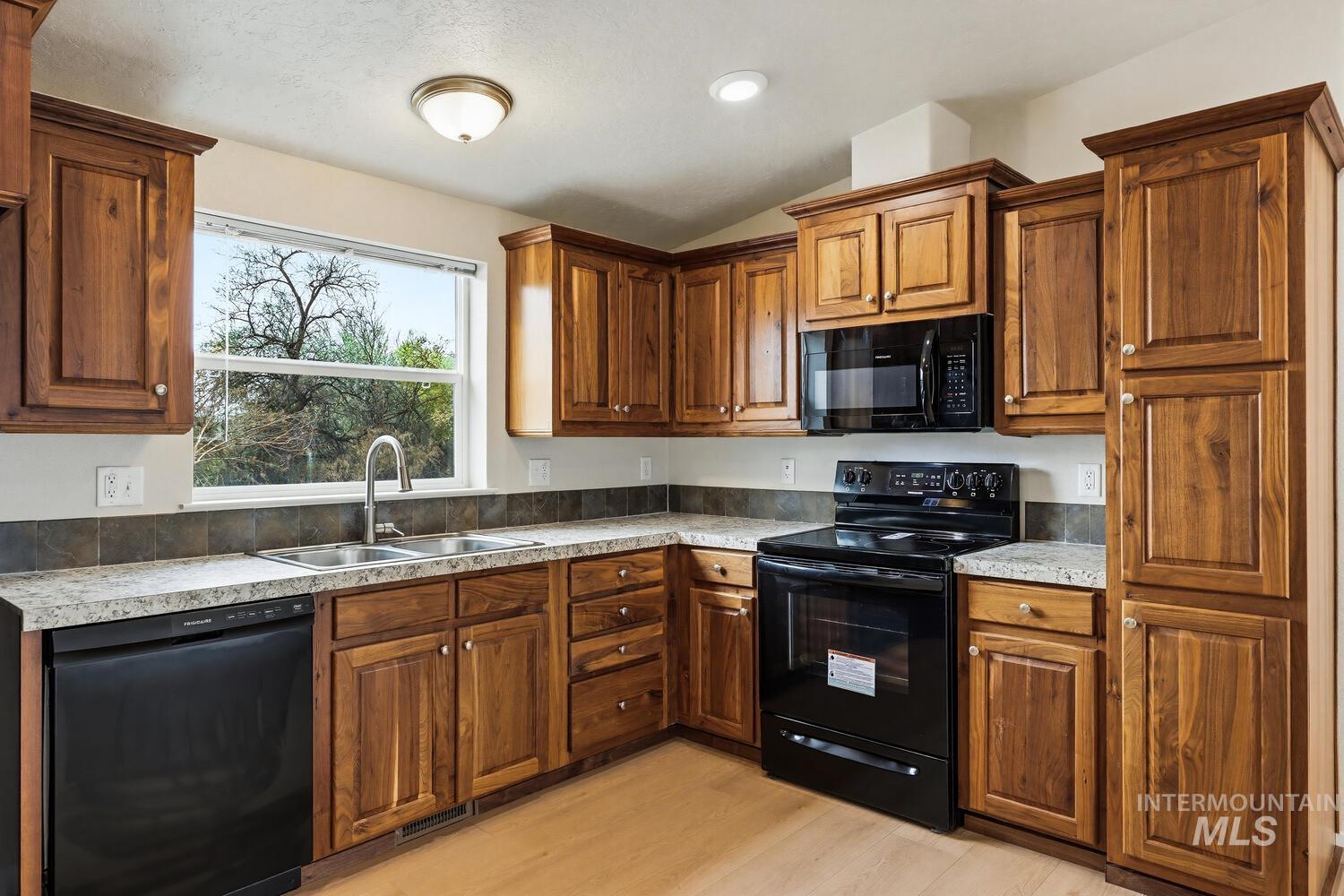 166 1st Street North Marsing, ID 83639 - Photo 12 of 37 Kitchen featuring black appliances, wood finish cabinetry, vaulted ceiling, light countertops, and light wood-type flooring