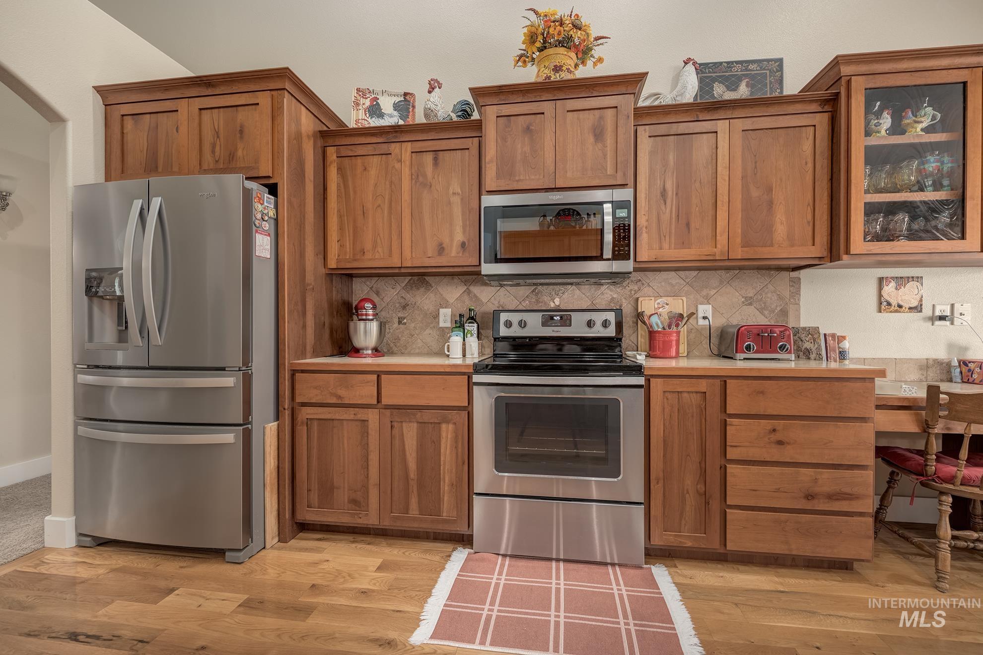 420 West Indianhead Road Weiser, ID 83672 - Photo 14 of 40 Kitchen featuring wood-finish flooring, custom wood cabinetry, stainless steel appliances, and a tiled backsplash