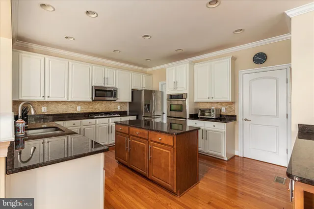 a kitchen with stainless steel appliances granite countertop a stove top oven a sink dishwasher and a refrigerator with wooden floor