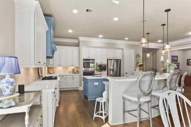 a kitchen with stainless steel appliances kitchen island granite countertop a refrigerator a stove a sink dishwasher and white cabinets with wooden floor