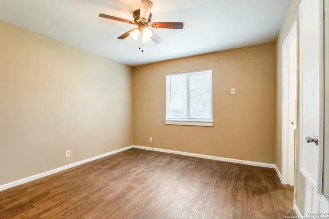 an empty room with wooden floor chandelier fan and windows