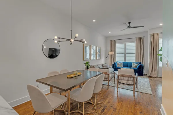 a living room with couches a dining table and a chandelier with wooden floor