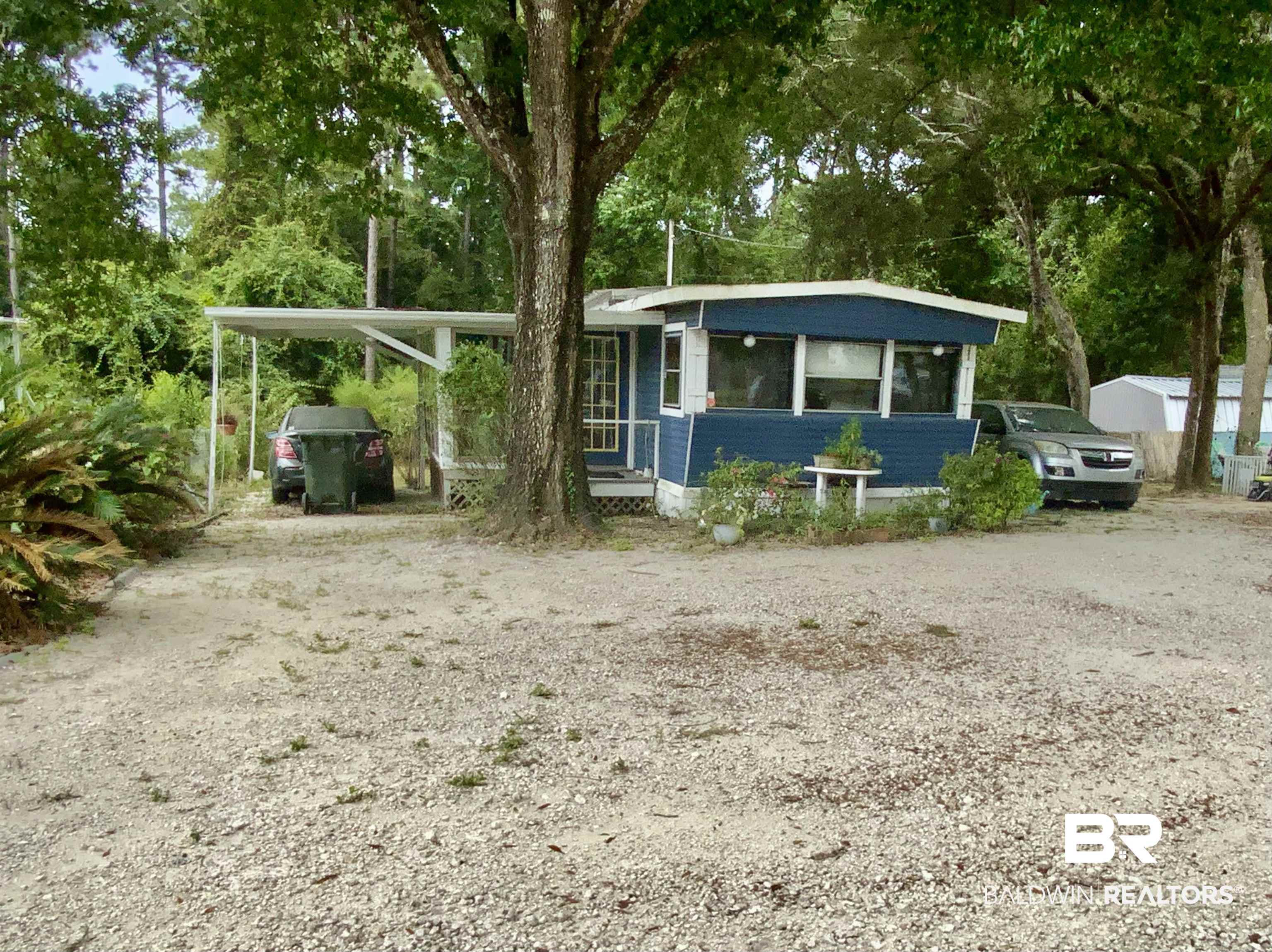 1413 Ridgewood Drive Lillian, AL 36549 - Photo 1 of 23 Manufactured / mobile home featuring a sunroom, dirt driveway, view of scattered trees, and an attached carport