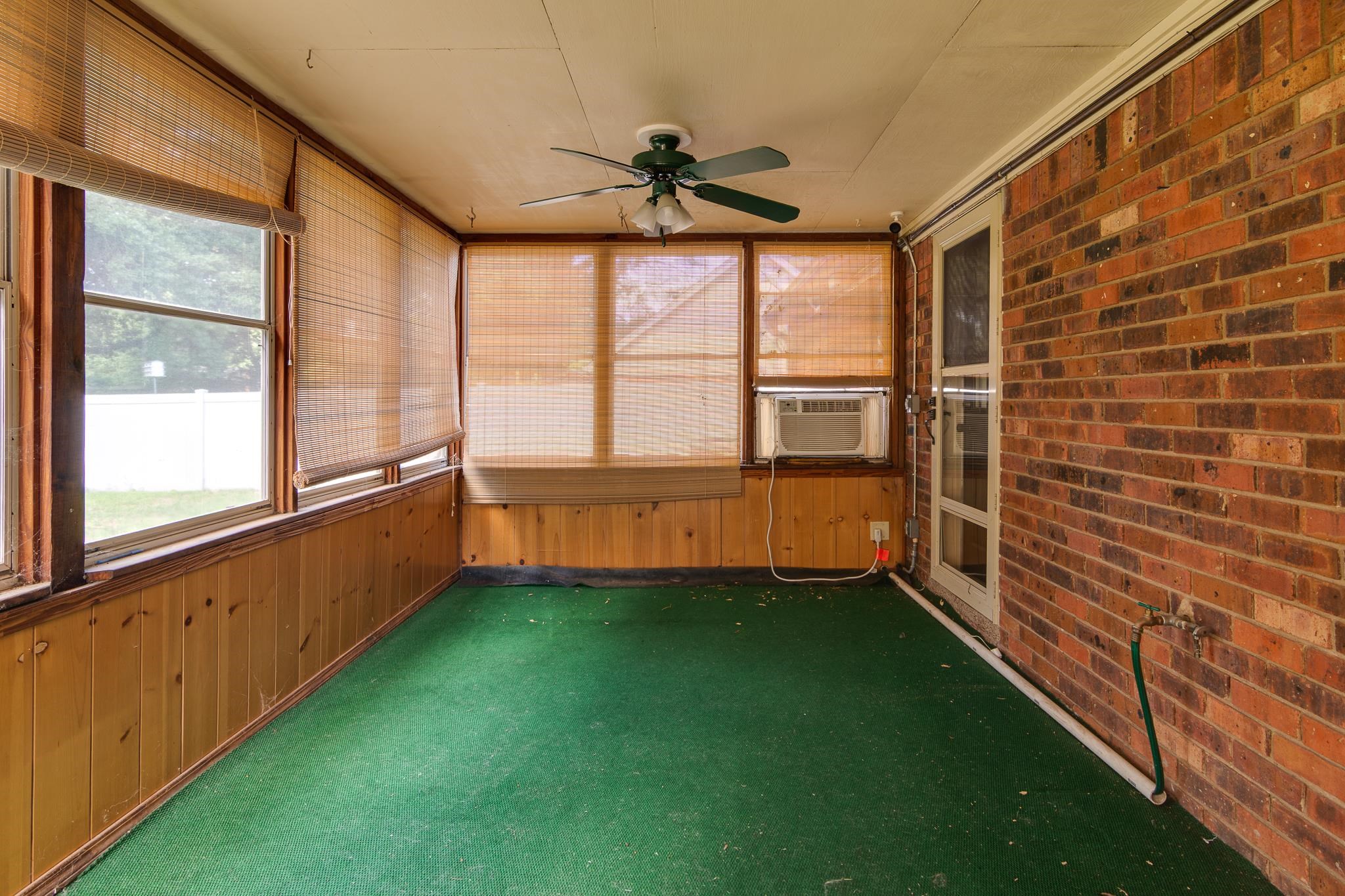 8083 Cinders Road Bartlett, TN 38133 - Photo 26 of 31 Enclosed sunroom featuring a brick wall, wood paneling, multiple windows with blinds, a ceiling fan, and green flooring