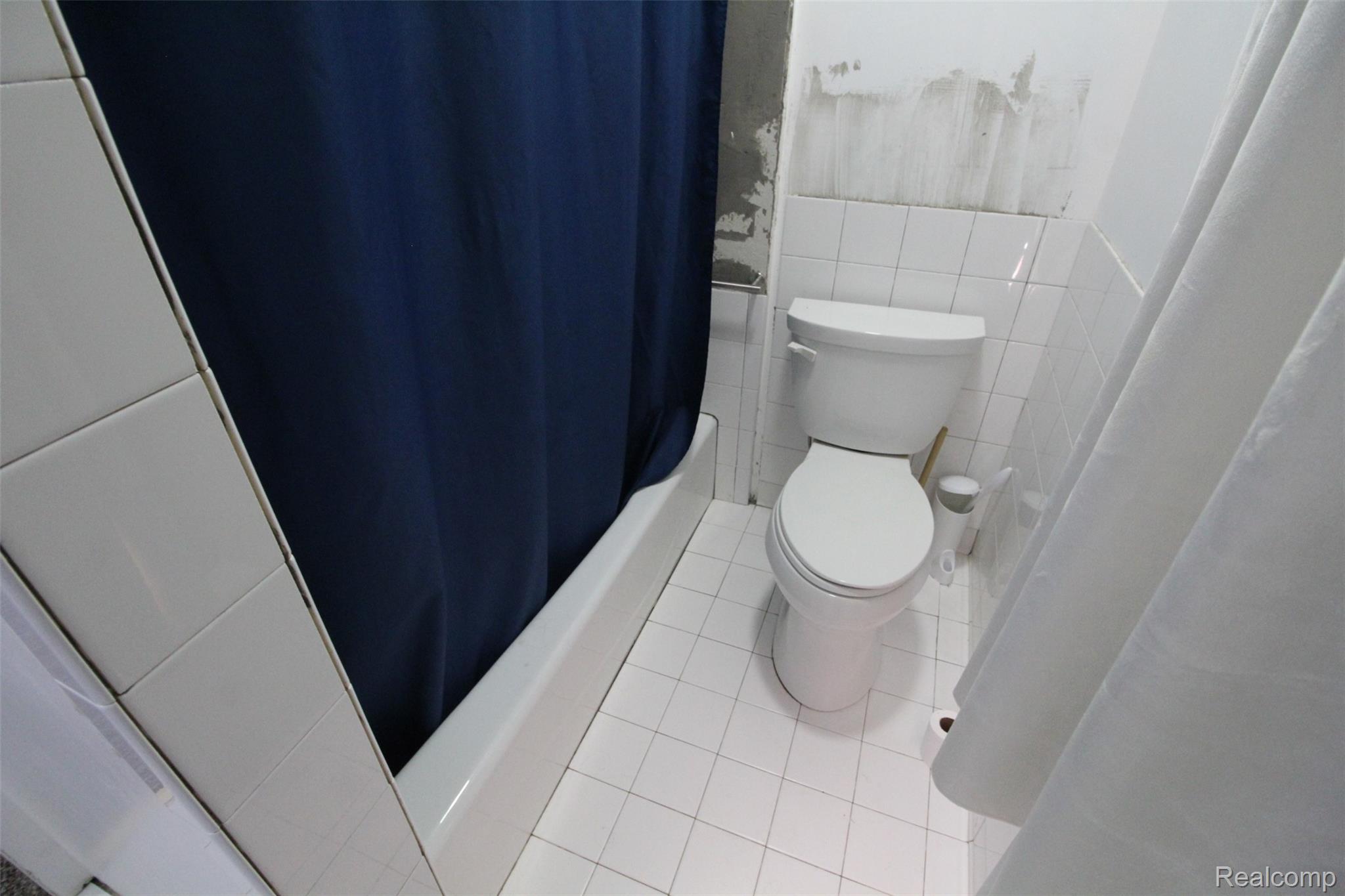 2568 Valentine Road Lapeer, MI 48446 - Photo 23 of 42 Compact bathroom featuring white ceramic tile flooring, white subway tile walls, a standard white porcelain toilet with seat, and a navy shower curtain enclosing the bathtub area