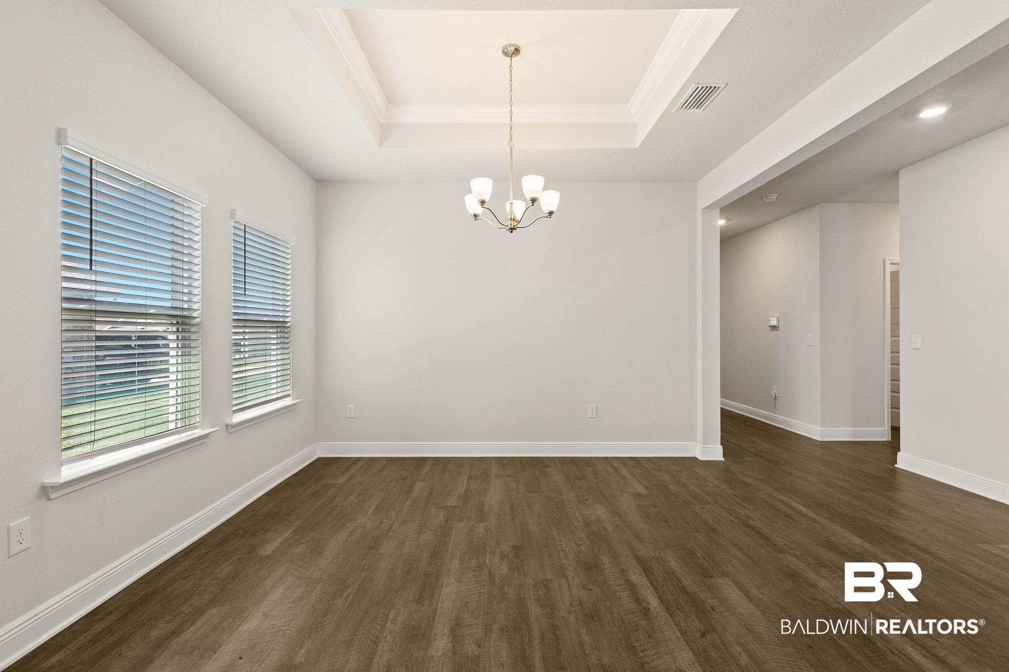 9448 Amethyst Drive Daphne, AL 36526 - Photo 13 of 61 Empty room featuring hanging lights, dark wood finished floors, a raised ceiling, and ornamental molding