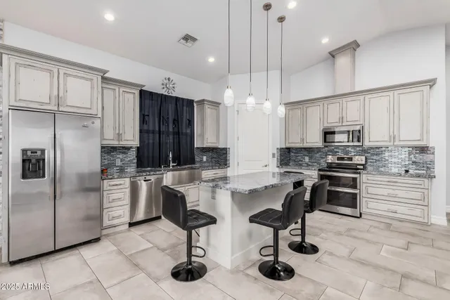 a kitchen with stainless steel appliances kitchen island granite countertop a stove a sink a refrigerator and chairs