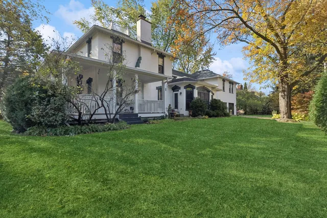 a view of a white house in front of a big yard with large trees