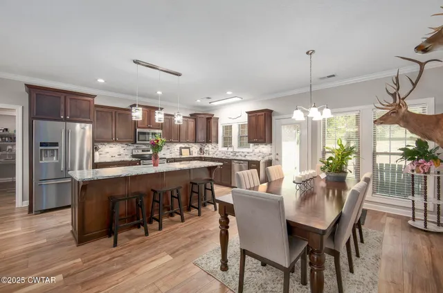 a kitchen with stainless steel appliances granite countertop wooden cabinets a stove a sink a dining table and chairs