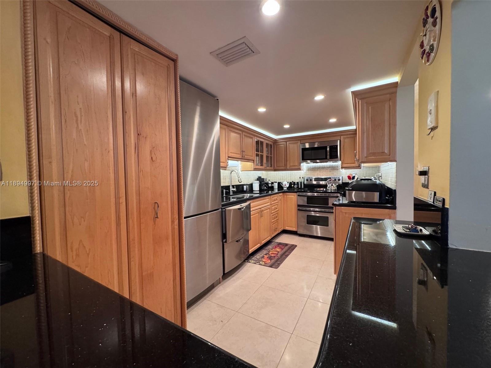 6061 Collins Avenue, Unit 10C Miami Beach, FL 33140 - Photo 21 of 45 a kitchen with stainless steel appliances granite countertop a refrigerator a stove and a sink with wooden floor