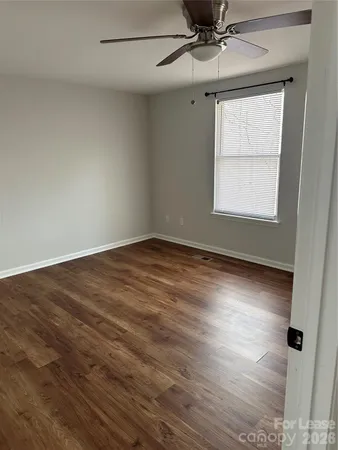 an empty room with wooden floor fan and windows