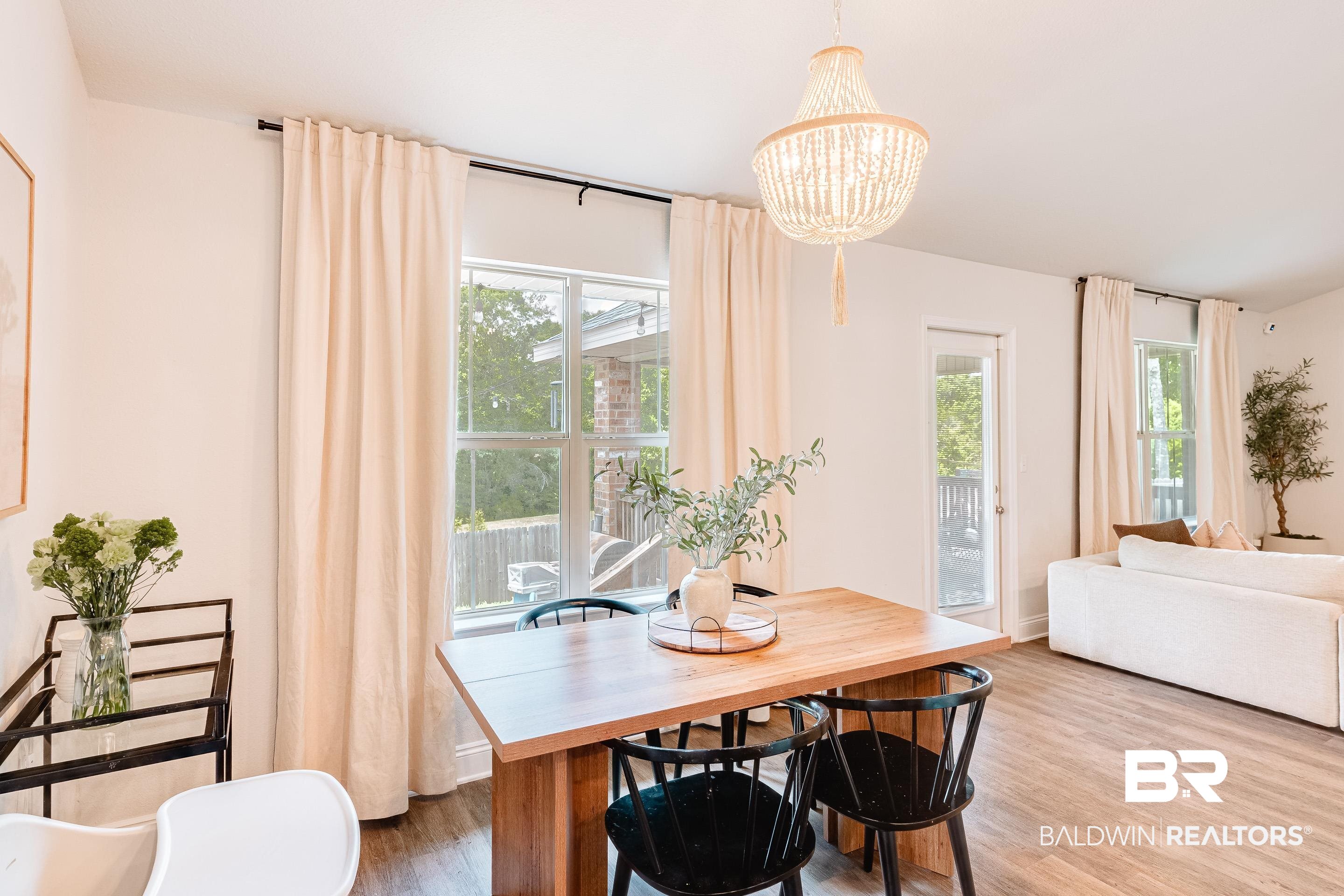 2215 Fernwood Loop West Semmes, AL 36575 - Photo 9 of 40 Dining area featuring a contemporary beaded chandelier, wood-finish flooring, two large windows with curtain rods, and a glass-paned exterior door