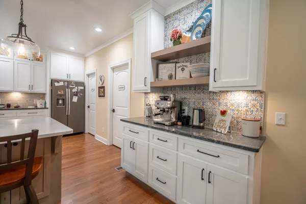 a kitchen with stainless steel appliances granite countertop a refrigerator a sink dishwasher and white cabinets with wooden floor