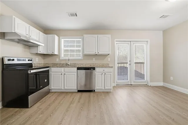 a kitchen with stainless steel appliances granite countertop a stove top oven a sink dishwasher and white cabinets with wooden floor