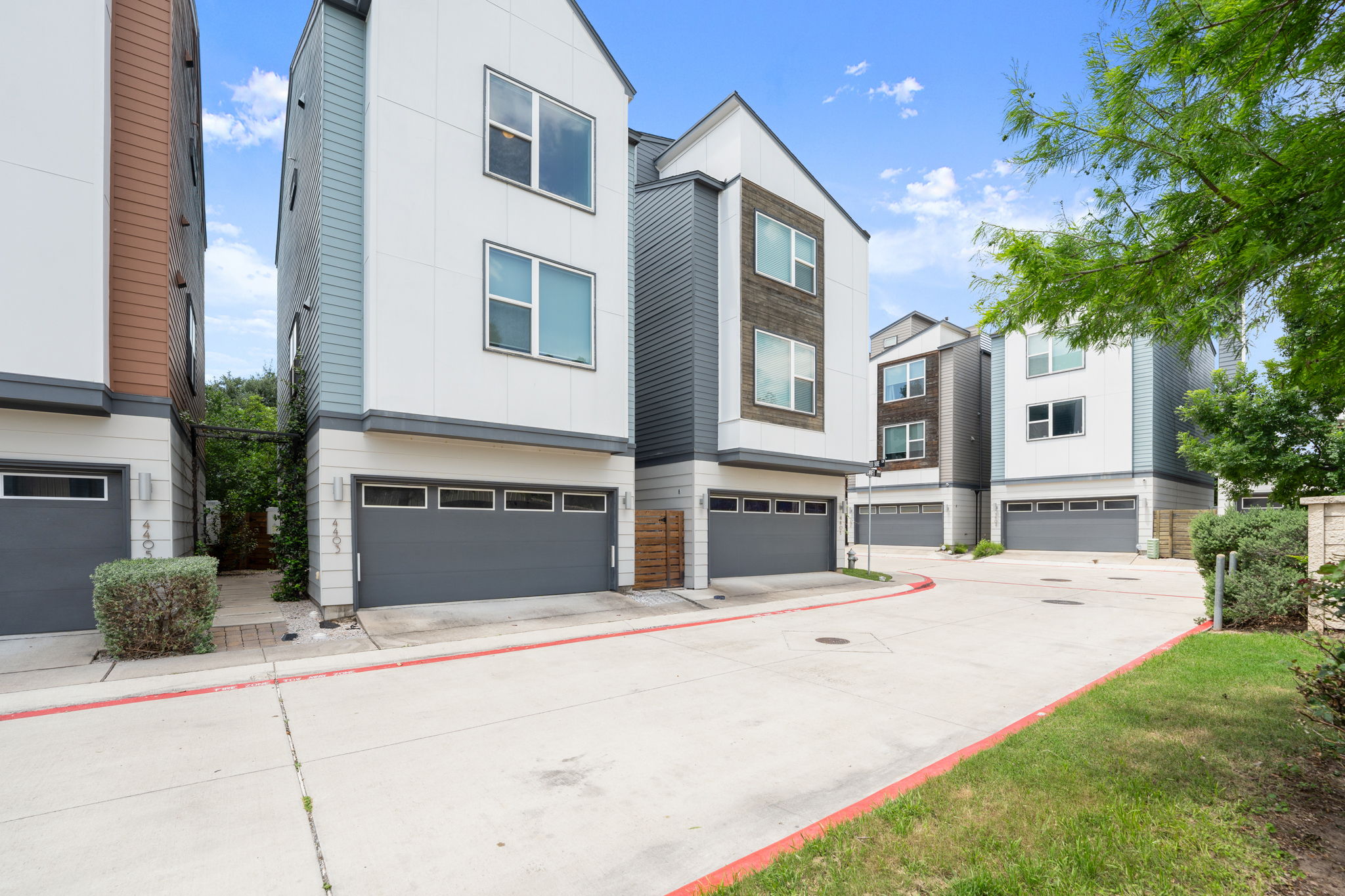 4403 Swift Path Austin, TX 78741 - Photo 2 of 32 Modern townhome exterior featuring a white facade with gray siding accents, wood-look paneling, a two-car garage with multiple transom windows, and a paved driveway