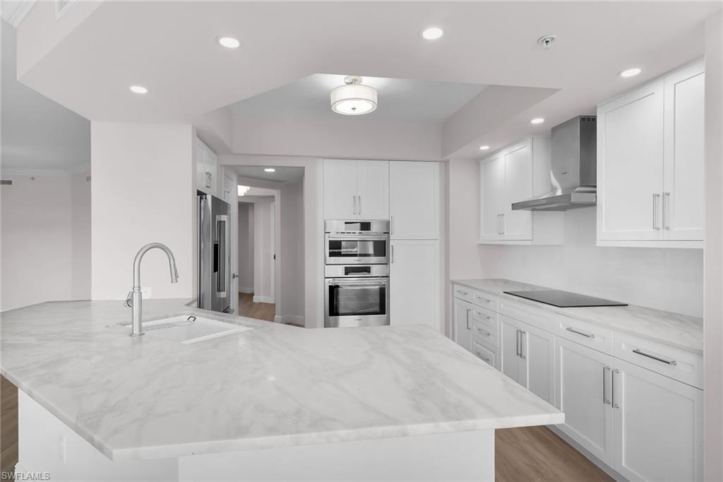 Kitchen with a peninsula, wall chimney exhaust hood, light wood-type flooring, light stone counters, and stainless steel appliances