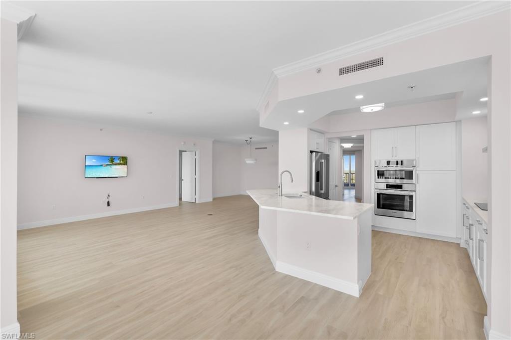 1060 Borghese Lane, Unit 803 Naples, FL 34114 - Photo 46 of 46 Kitchen featuring white cabinets, open floor plan, light wood finished floors, ornamental molding, and stainless steel appliances