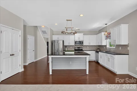 a open kitchen with granite countertop a stove top oven a chimney cabinets and wooden floor