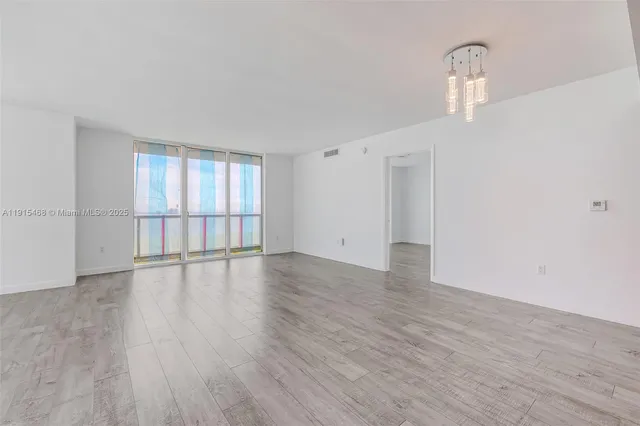 a view of an empty room with wooden floor and fan