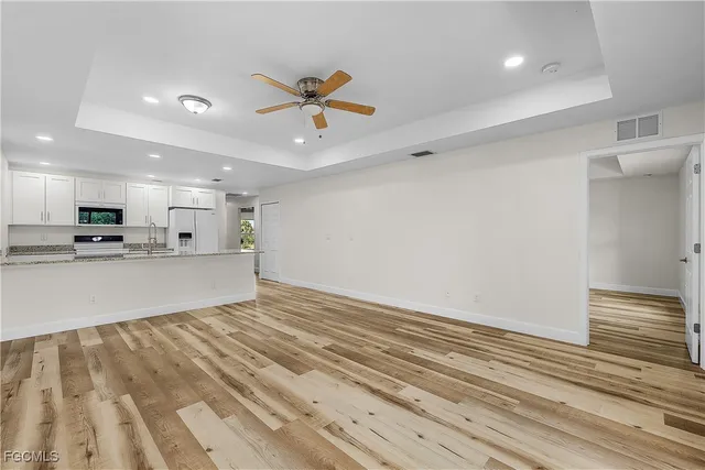a view of an empty room and kitchen view with wooden floor