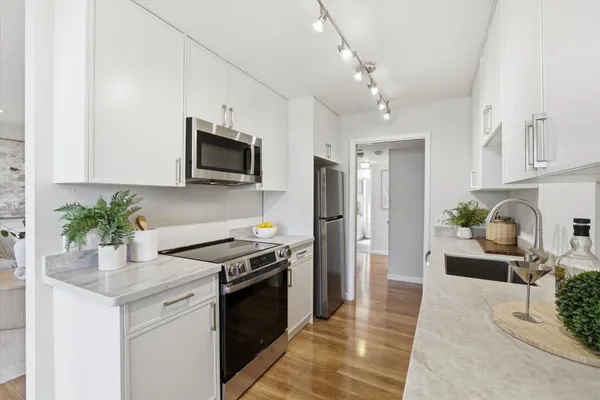a kitchen with stainless steel appliances granite countertop a refrigerator a stove a sink dishwasher and white cabinets with wooden floor