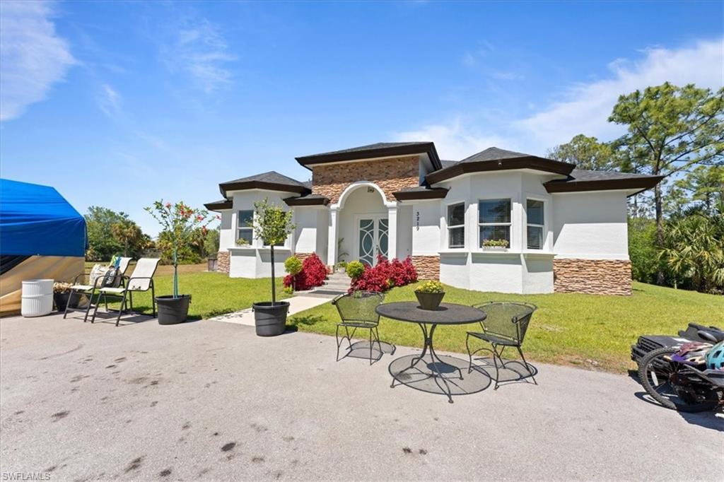 3219 64th Avenue Northeast Naples, FL 34120 - Photo 2 of 33 Back of property with stucco siding, stone siding, a yard, and a patio area