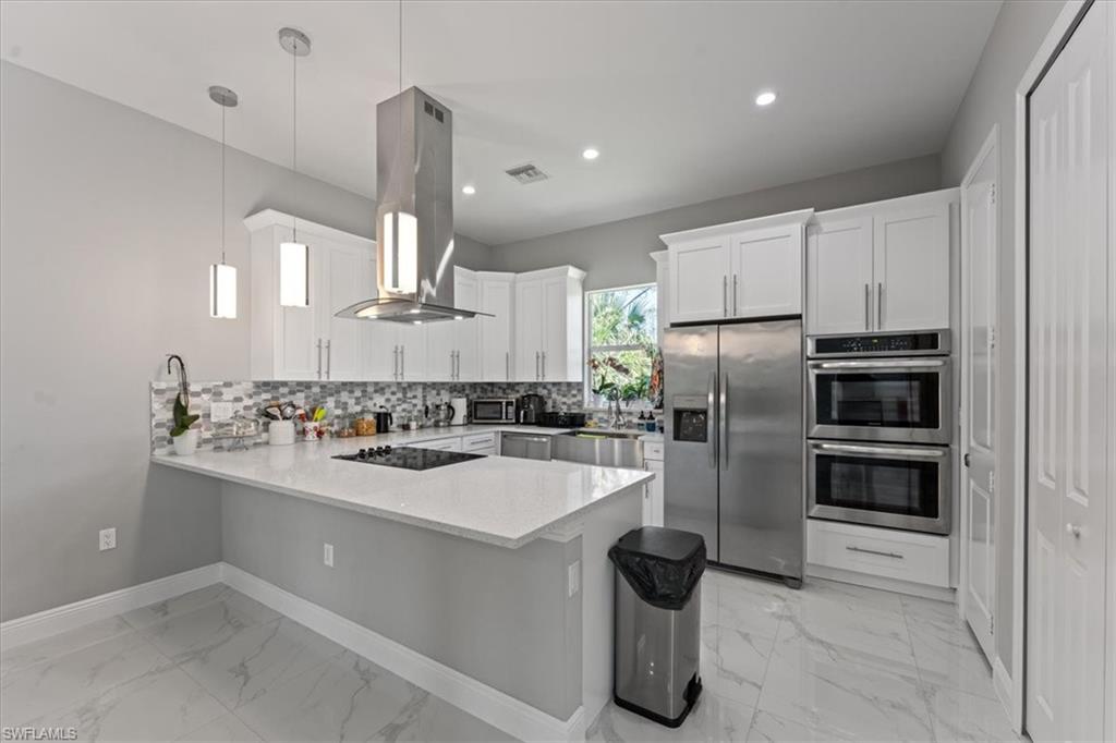3219 64th Avenue Northeast Naples, FL 34120 - Photo 8 of 33 Kitchen with tasteful backsplash, appliances with stainless steel finishes, island exhaust hood, a peninsula, and marble finish floor