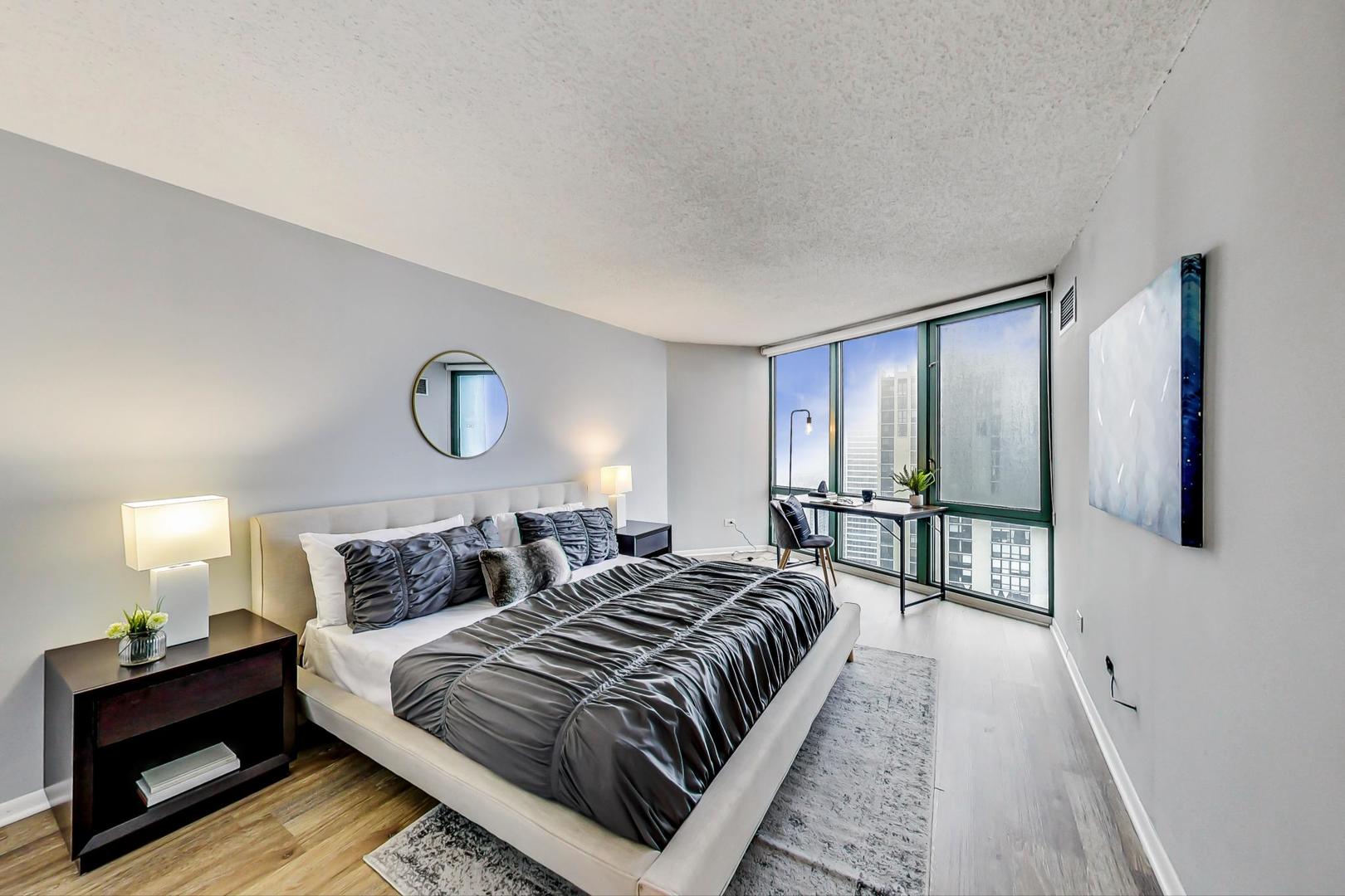 111 West Maple Street, Unit 3005 Chicago, IL 60610 - Photo 10 of 18 a bedroom with a bed a mirror on dresser and a window