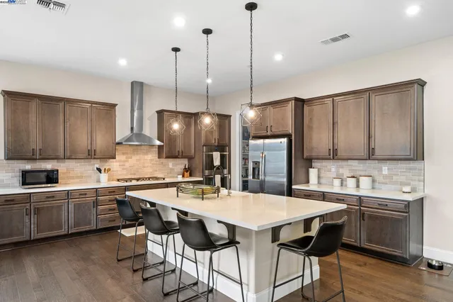 a kitchen with stainless steel appliances kitchen island granite countertop a sink a stove a refrigerator and island with wooden floor